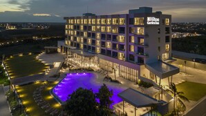 Een modern hotel met een zwembad, meerdere verdiepingen en een goed verlichte gevel.