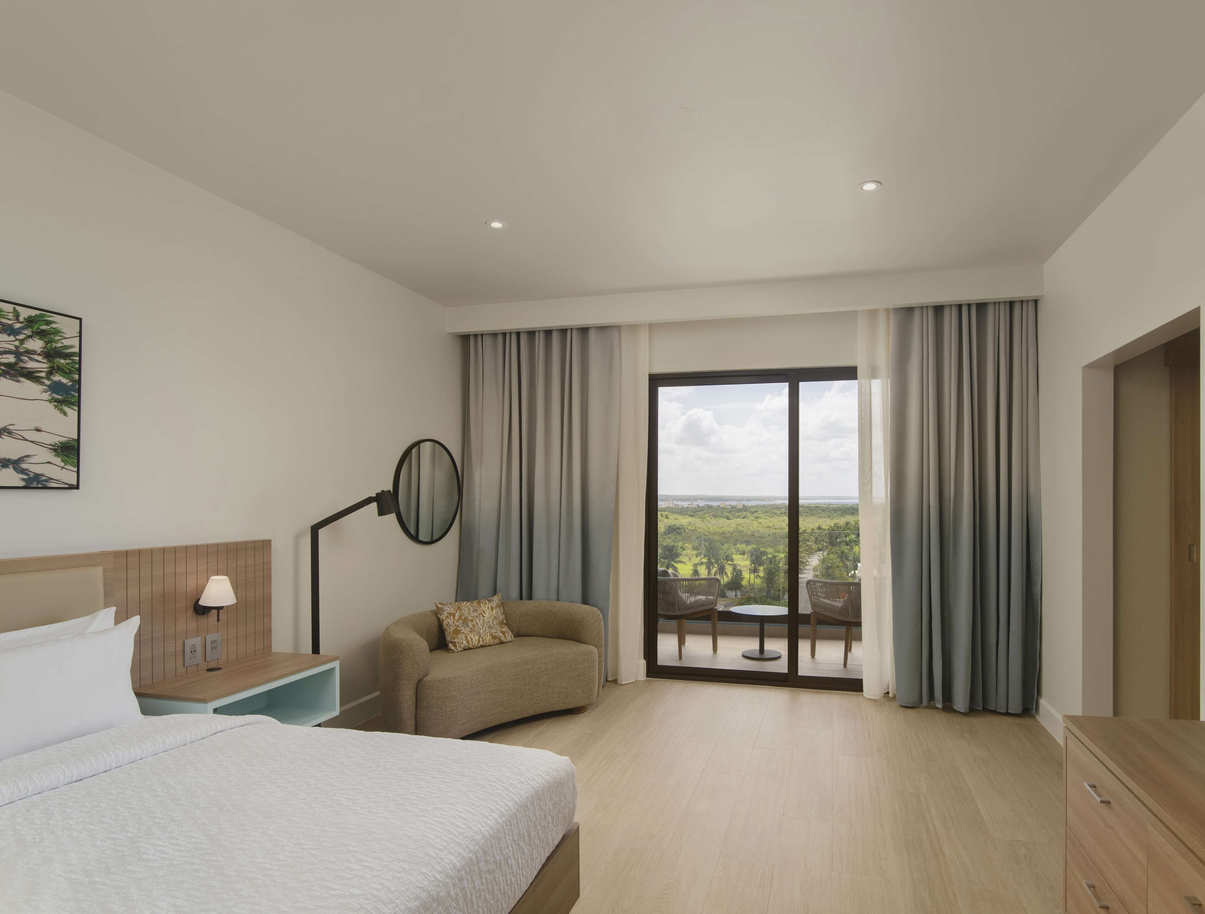 A hotel room with a bed, a desk, a chair, a round table, and a balcony with curtains.