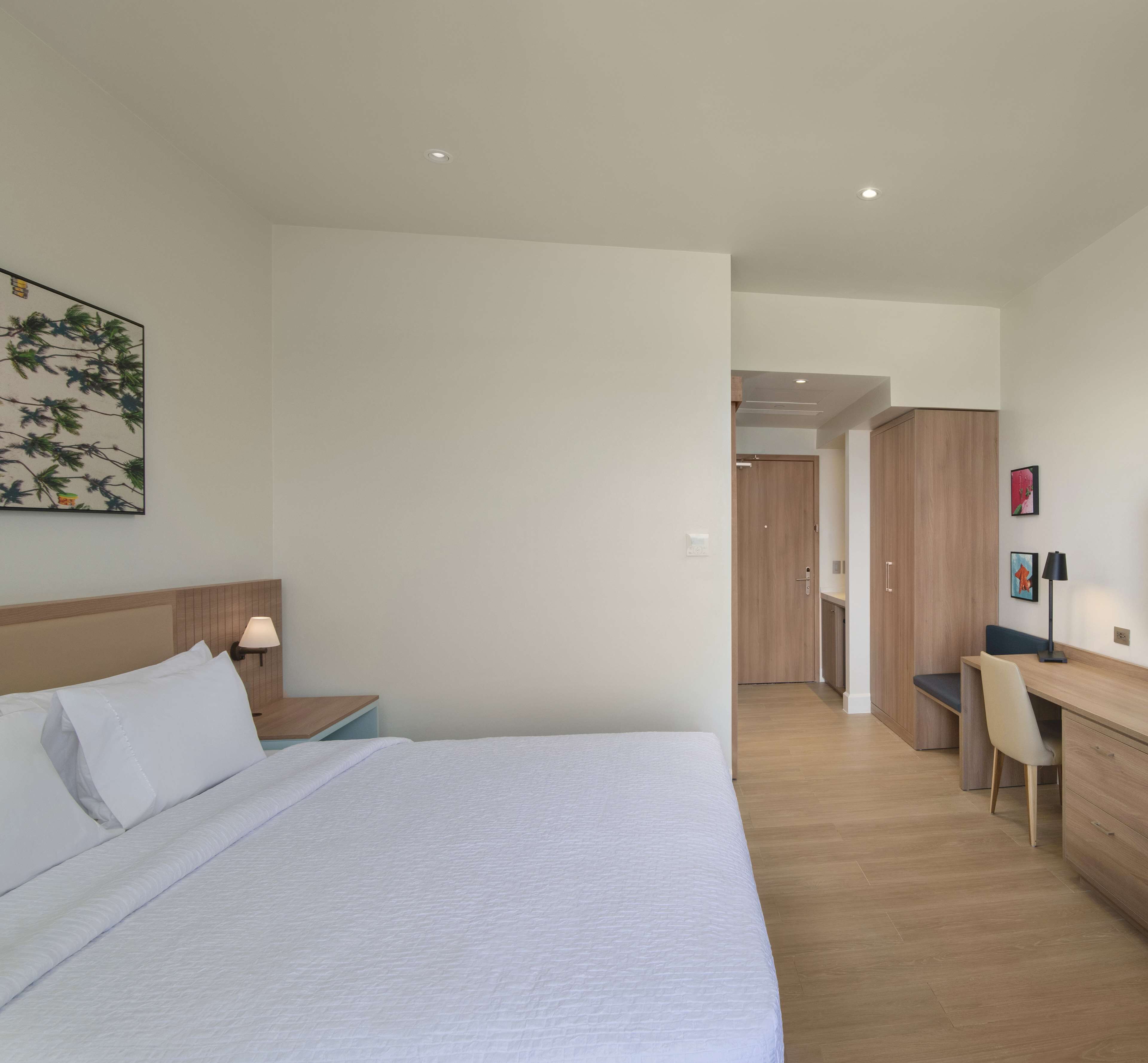 A modern hotel room with a large bed, a desk, and a wardrobe.