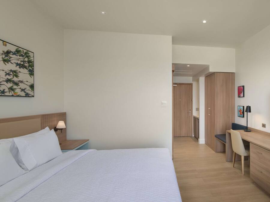 A modern hotel room with a large bed, a desk, and a wardrobe.