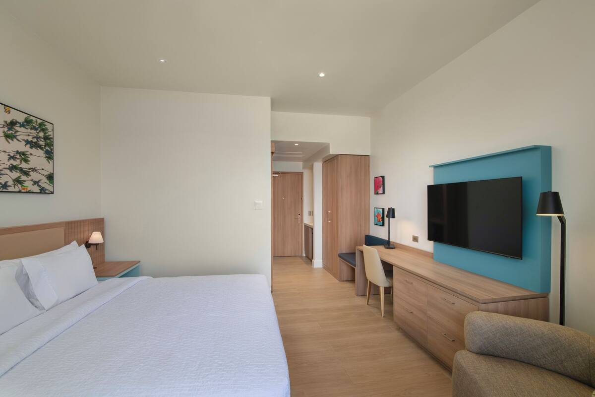 Une chambre d’hôtel avec un lit, un bureau, une chaise, une télévision et une lampe.