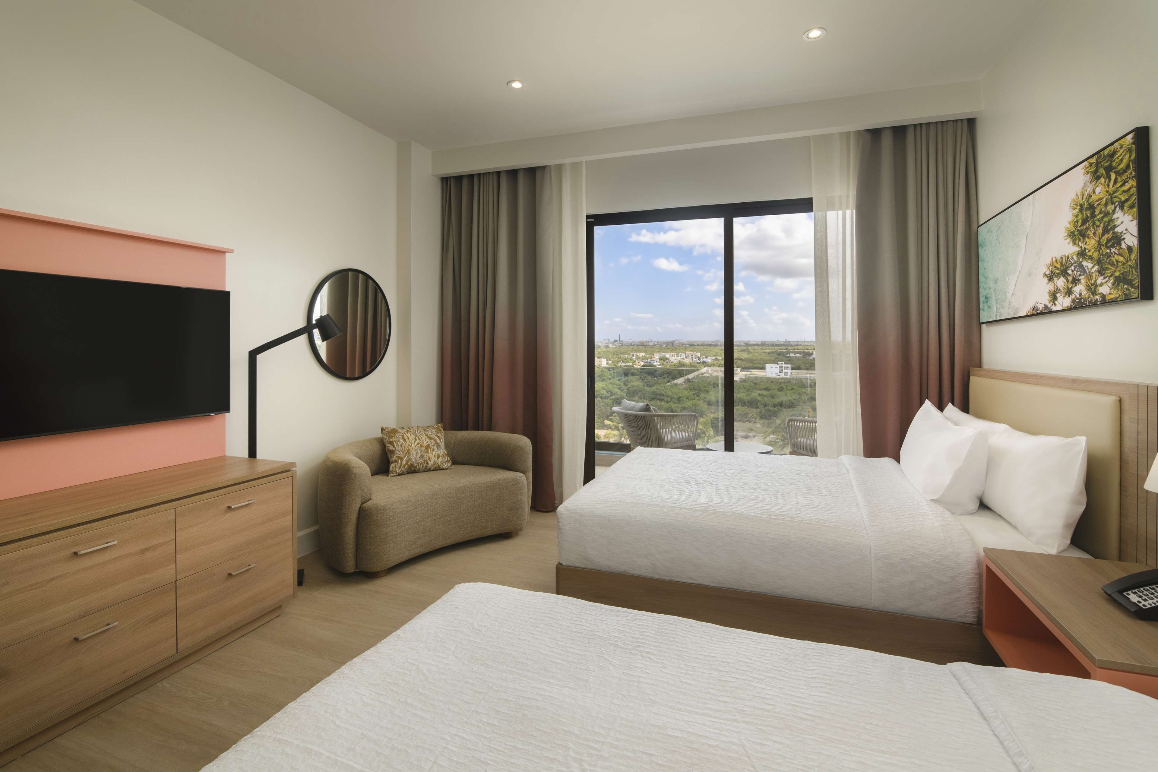 A hotel room with two beds, a sofa, a TV, and a large window with a city view.