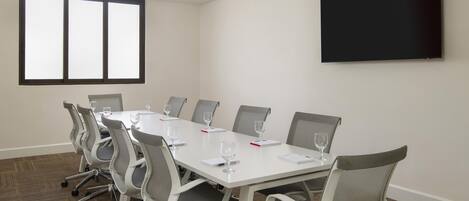 A conference room with a long table, chairs, a flat-screen TV, and a large window.