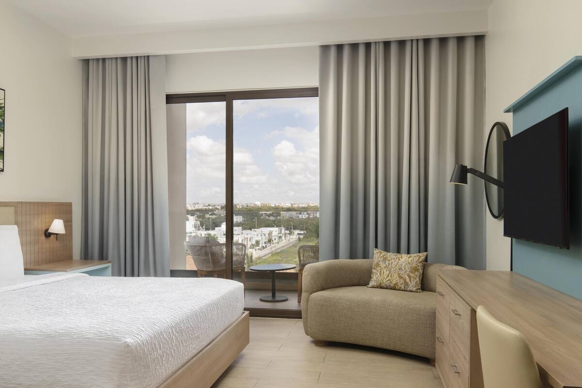 Une chambre d’hôtel avec un lit, un canapé, une télévision, un bureau, une lampe et une vue sur la ville.