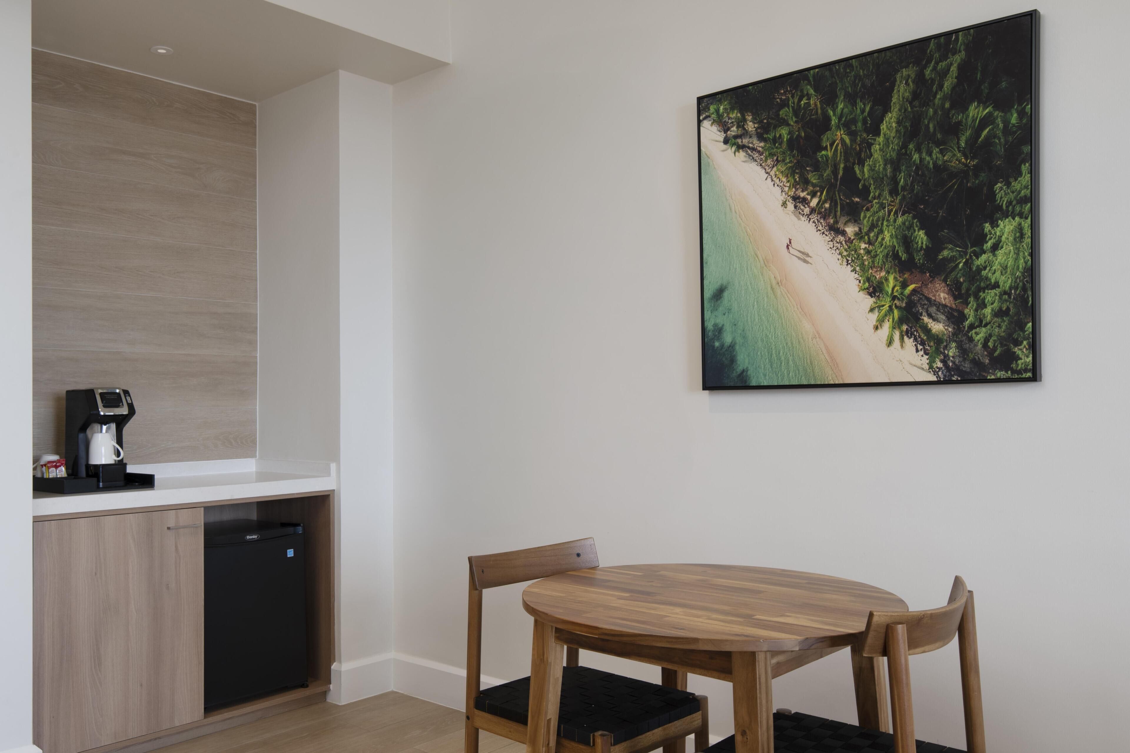 Een keuken met een koffieapparaat, een vaatwasser en een eethoek met een houten tafel en stoelen.