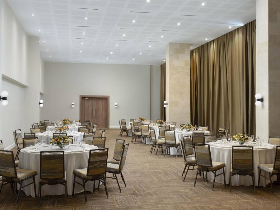 Un amplio salón de banquetes con mesas redondas dispuestas para el servicio de comidas, con sillas y vajilla.