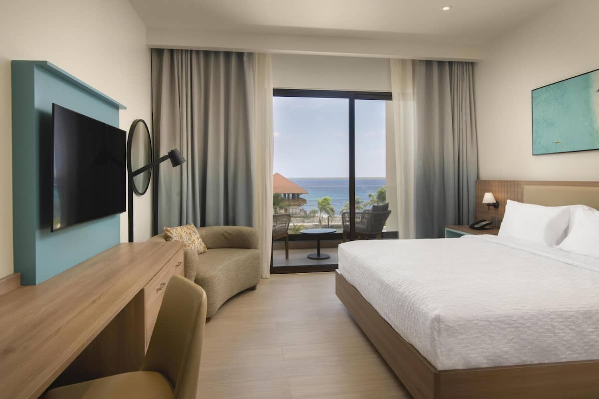 Une chambre d’hôtel avec un lit, un bureau, une télévision, une chaise, une table et une vue sur l’océan.