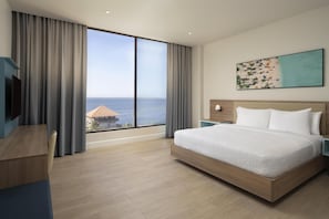Una habitación de hotel con un ventanal grande, una cama, un escritorio y un cuadro.