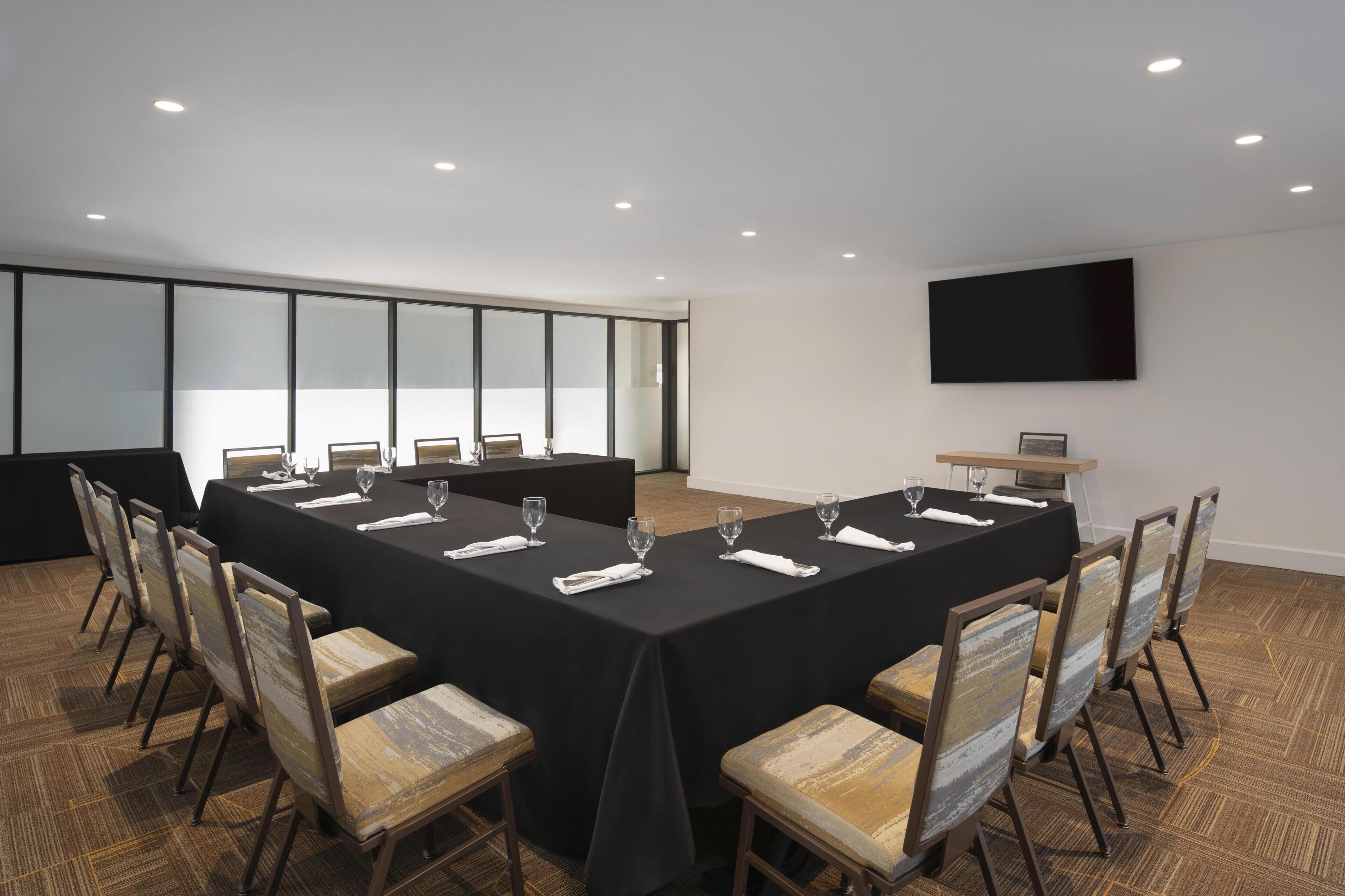 Un salón de conferencias con una larga mesa, sillas y un televisor de pantalla plana en la pared.