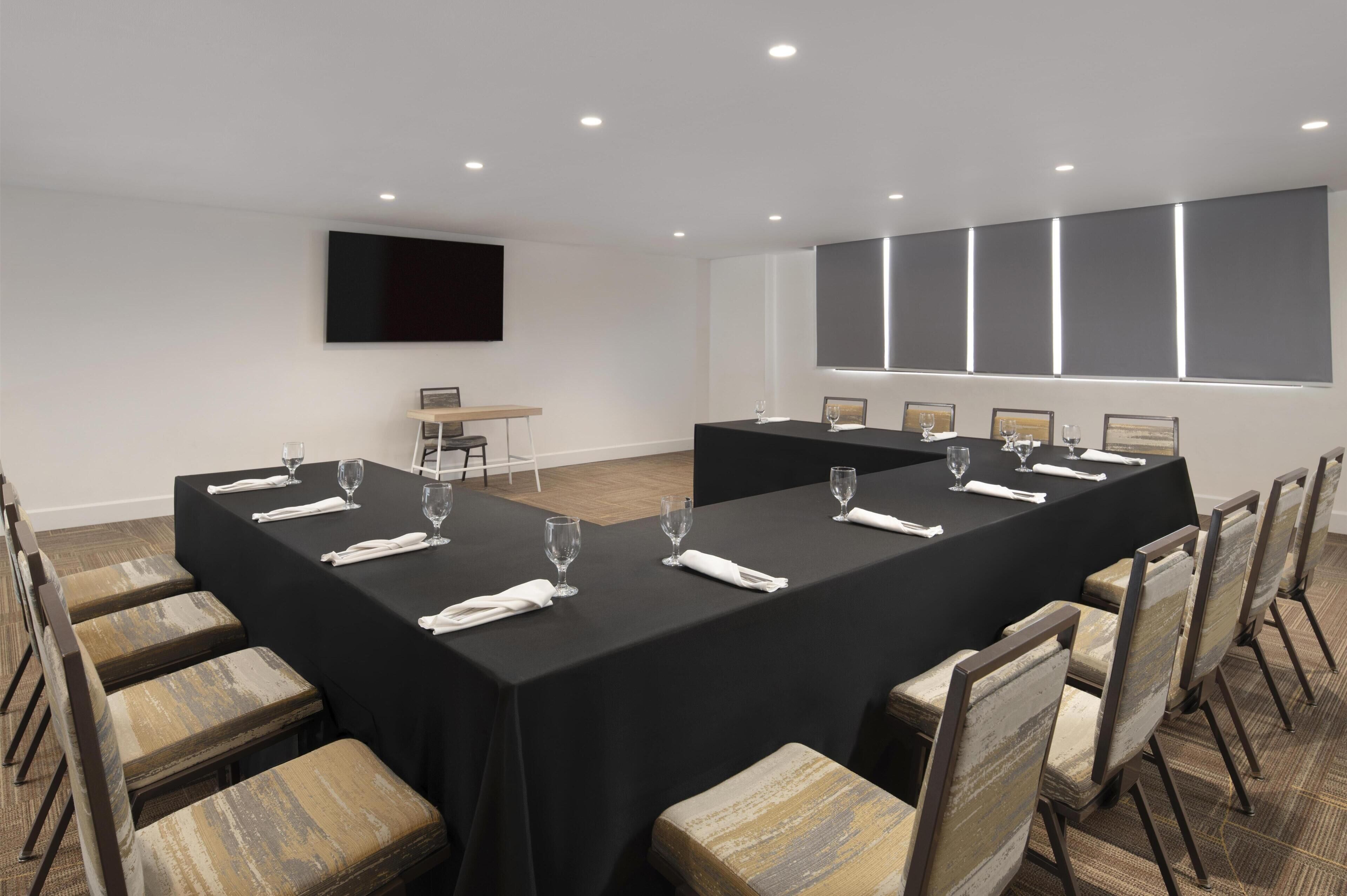 Un salón de conferencias con una larga mesa, sillas y una pantalla de televisión.