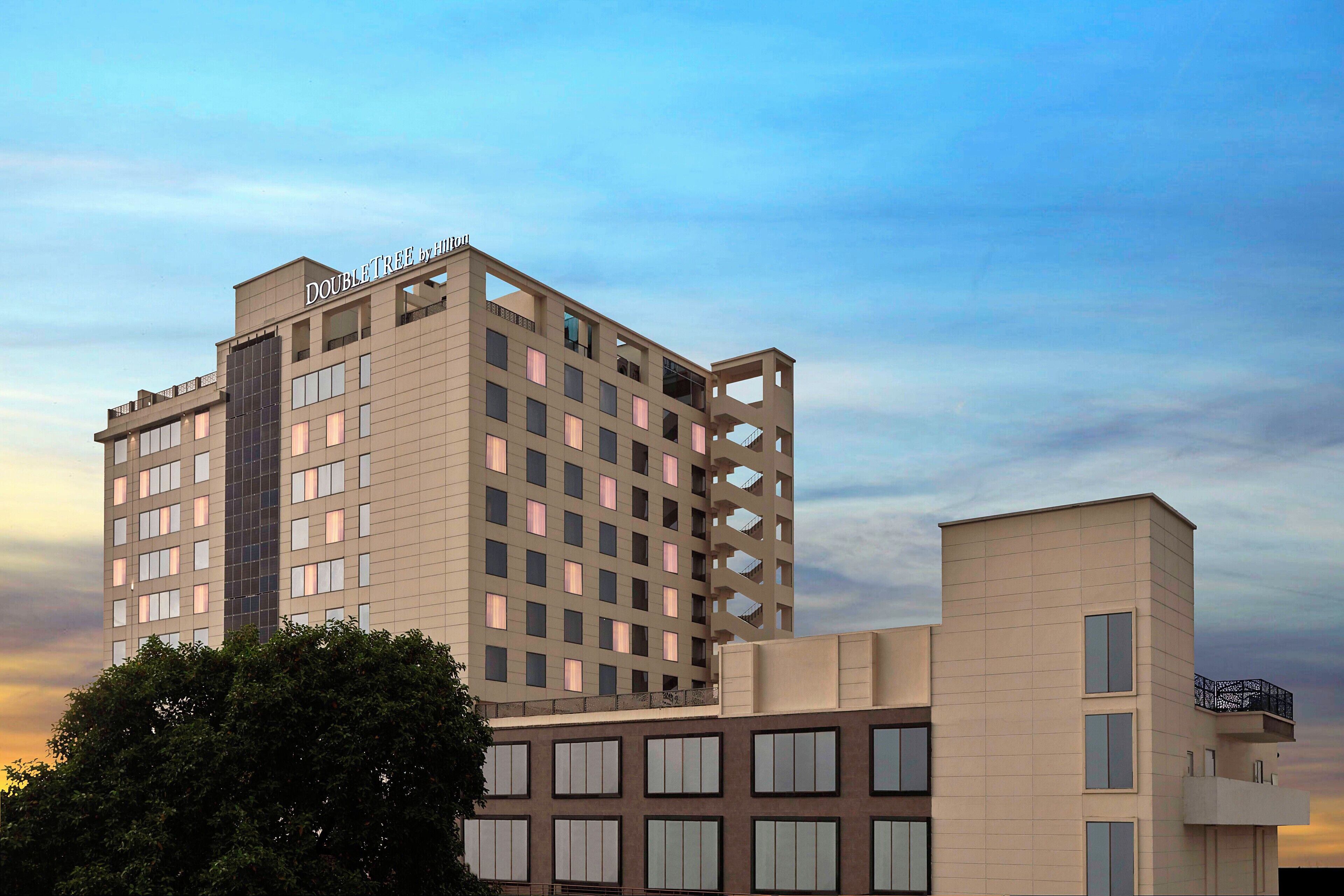 A modern hotel with a prominent "DOUBLETREE by Hilton" sign, featuring a grid of windows and balconies on the upper floors.