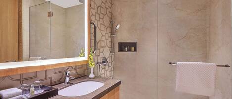 Un baño moderno con un espejo grande, un lavabo de mármol, una ducha con puerta de cristal y un perchero para toallas.
