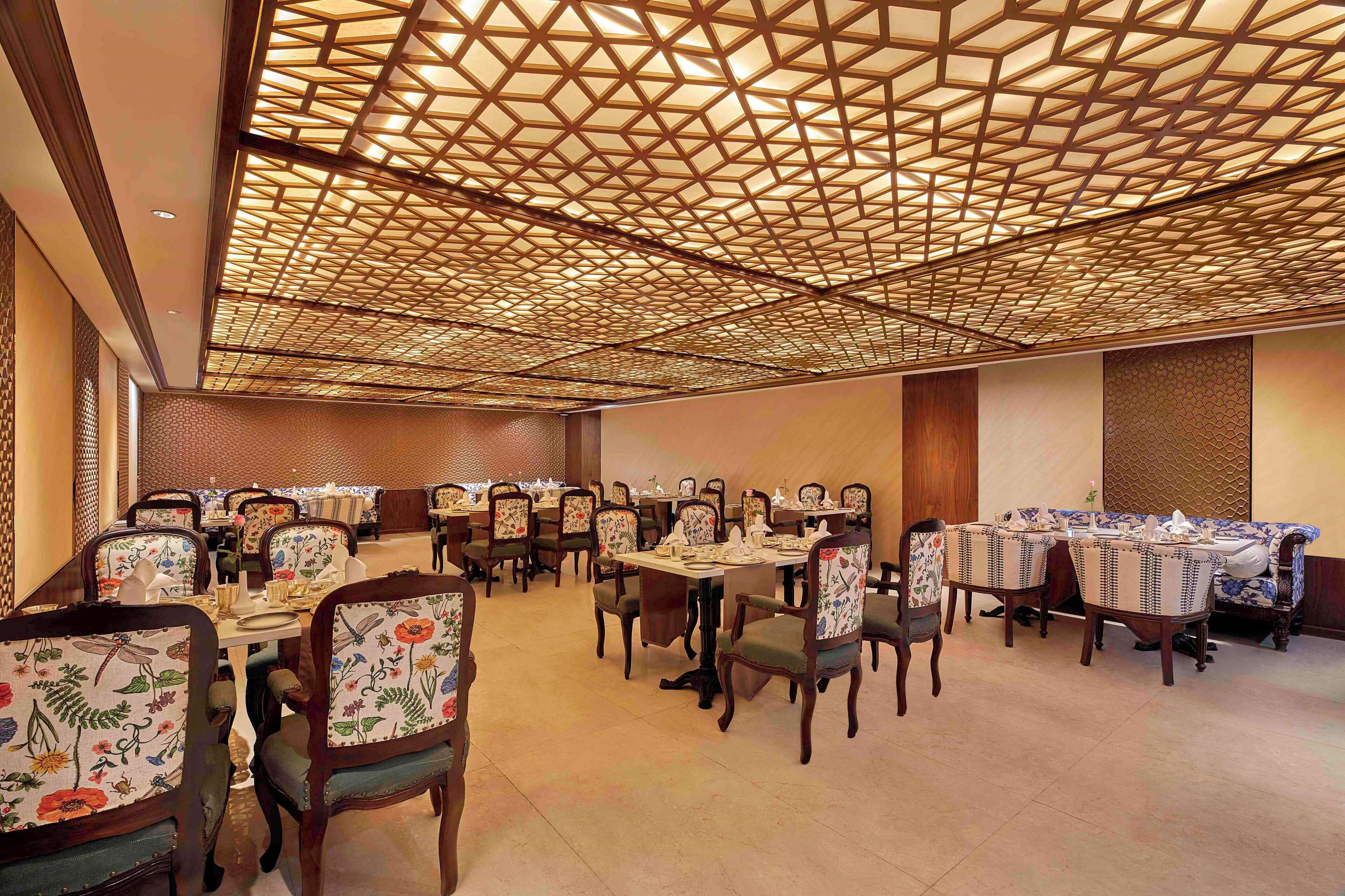 A dining area with multiple tables and chairs, featuring a geometric patterned ceiling and traditional decor.