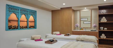 A spa room with two beds, a wooden cabinet, a mirror, and a decorative wall piece.