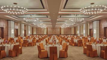 Un gran salón de banquetes con varias mesas redondas, cada una con manteles blancos y sillas anaranjadas.