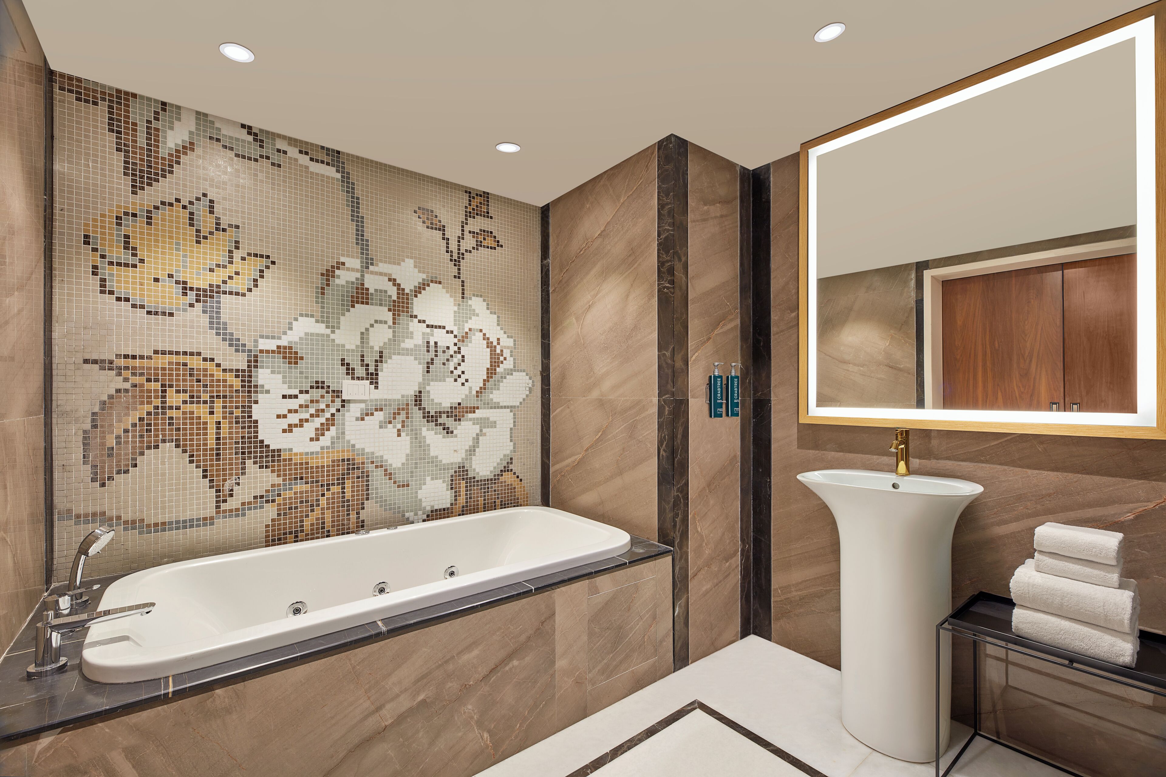 A modern bathroom with a freestanding bathtub, a pedestal sink, and a mosaic wall.