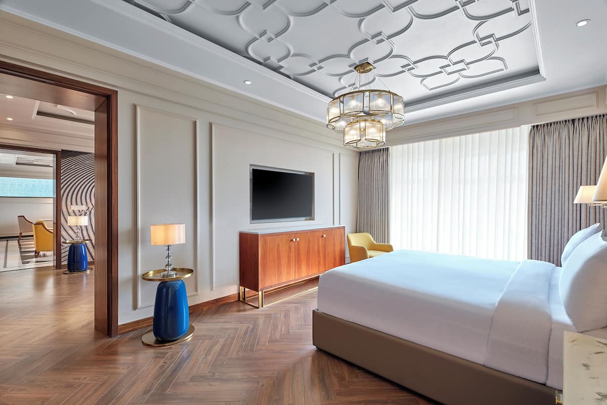 Una habitación de hotel con una cama grande, un televisor, un armario de madera y una lámpara de pie azul.