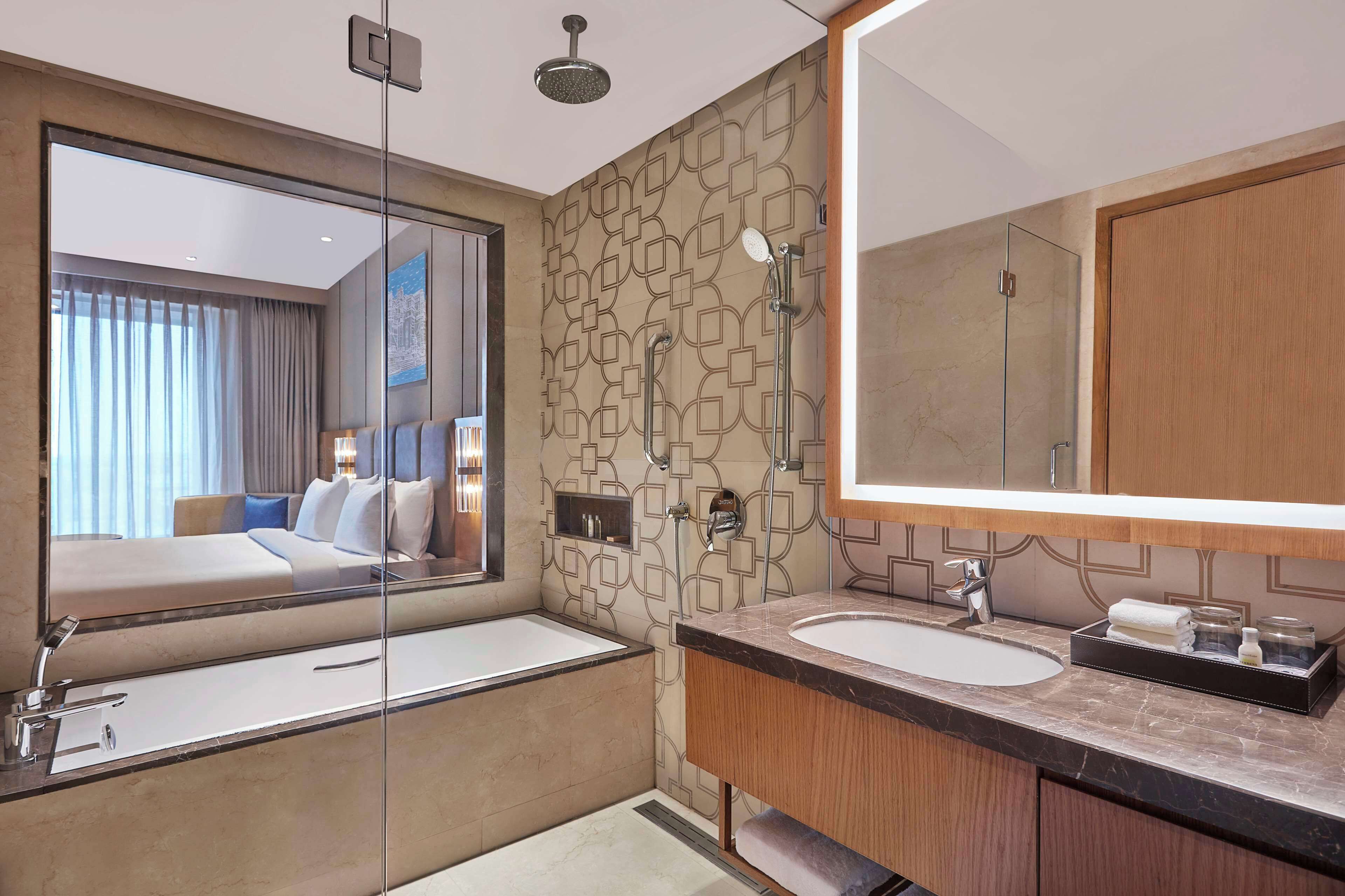 Une salle de bain d’hôtel moderne, dotée d’un grand miroir, de deux vasques, d’une douche et d’un espace de douche clos par des parois de verre.