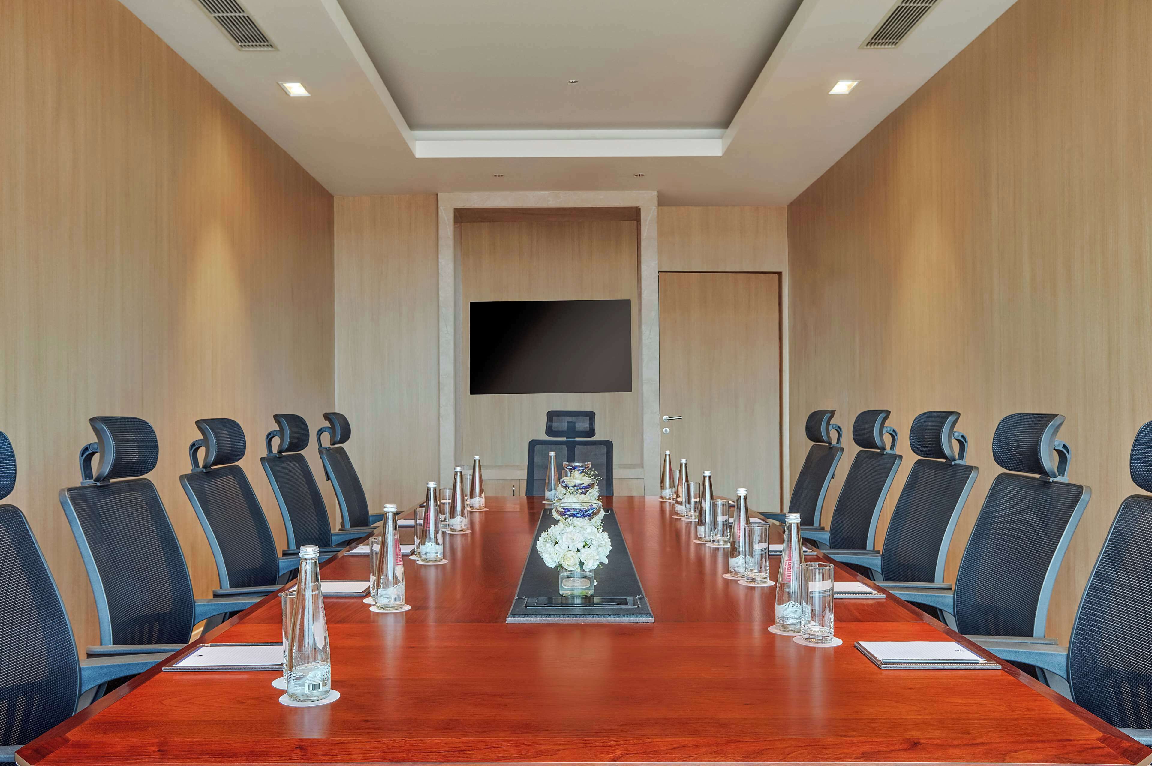 A conference room with a long table, chairs, a TV screen, and a floral centerpiece.