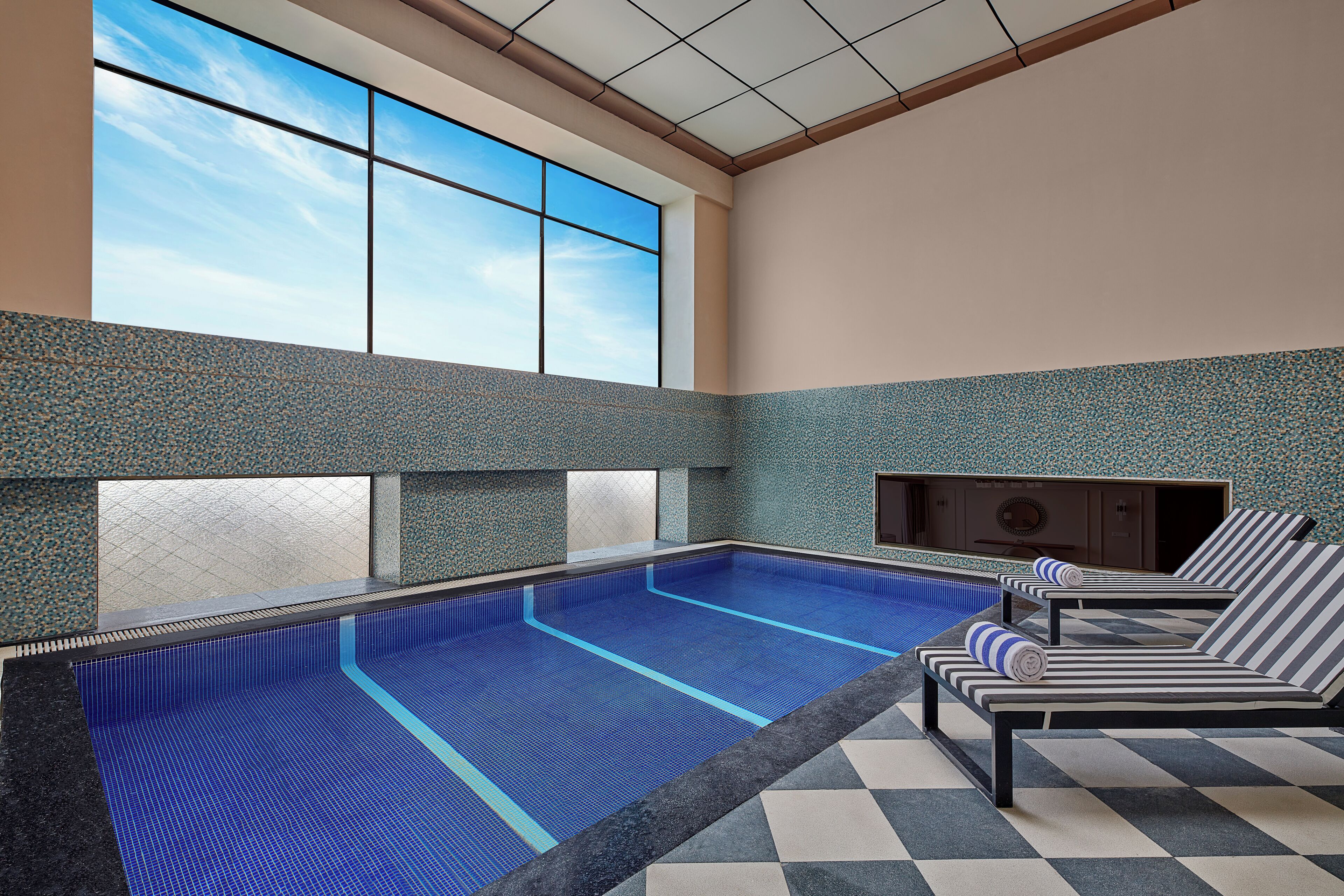 Piscina interior con sillas de descanso y un ventanal grande.