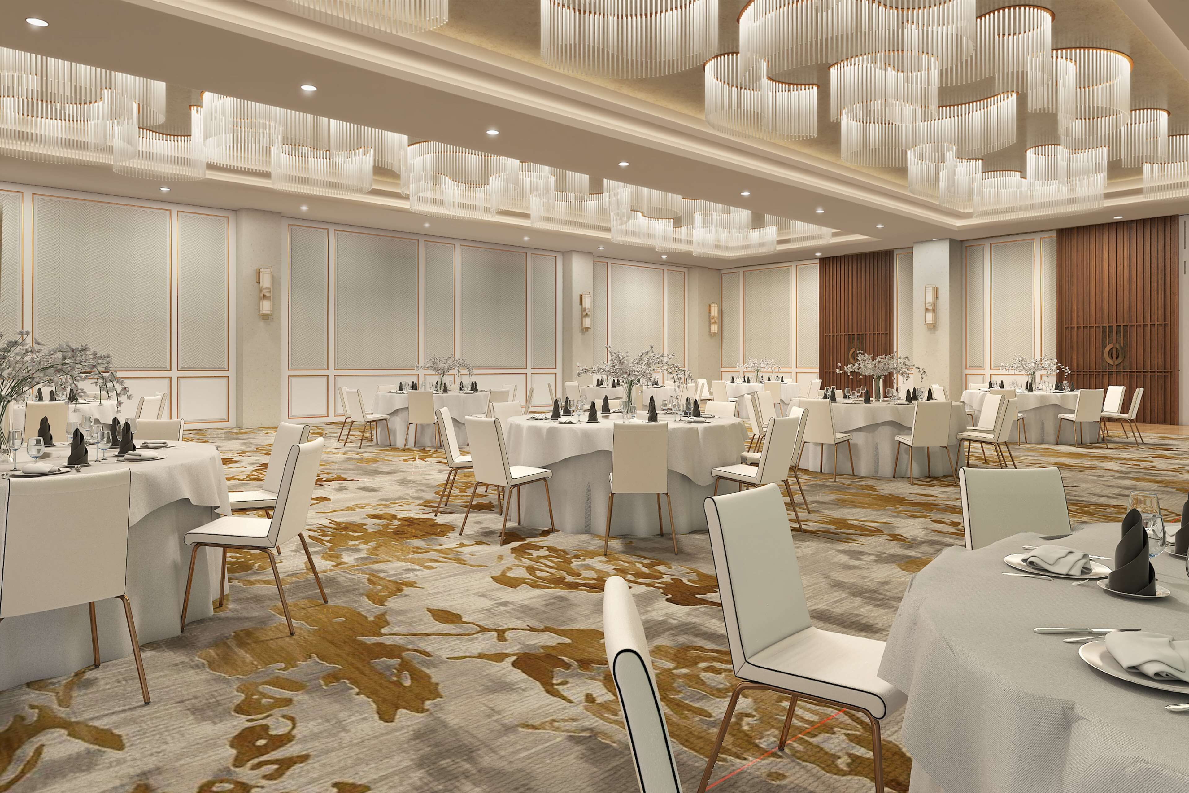 A spacious banquet hall with round tables, white chairs, and chandeliers.