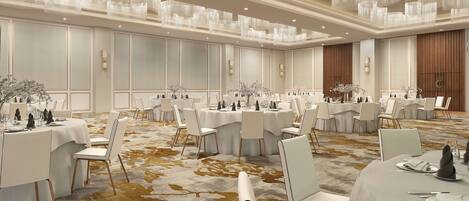 A spacious banquet hall with round tables, white chairs, and chandeliers.