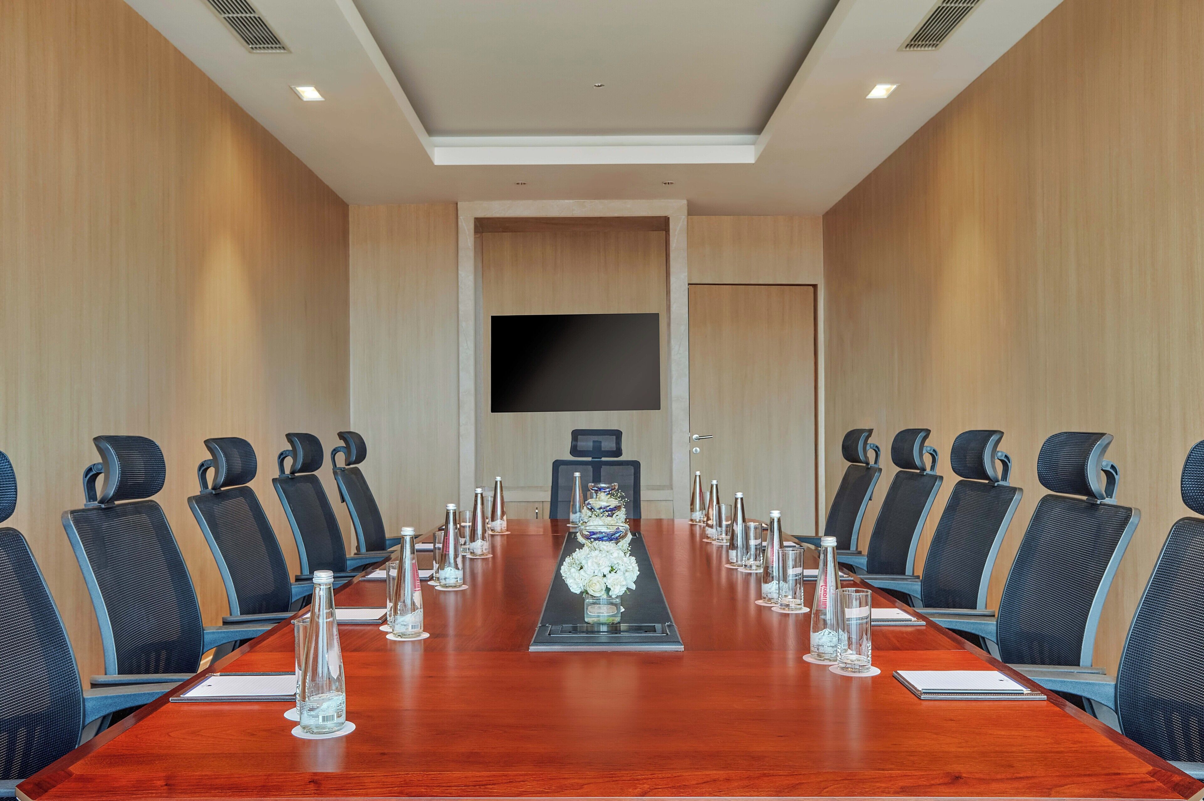 A conference room with a long table, black chairs, and a large screen at the front.