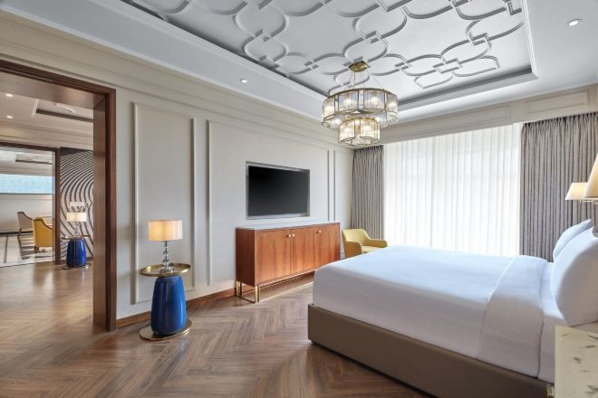 Una habitación de hotel con una cama grande, un televisor, un armario de madera y una araña.