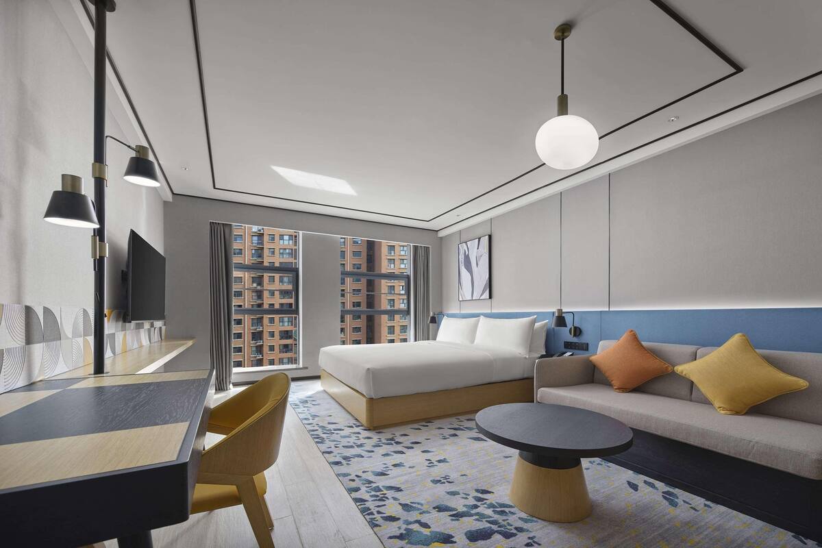 Una habitación de hotel moderna con una cama grande, un sofá, una mesa de comedor y un televisor.