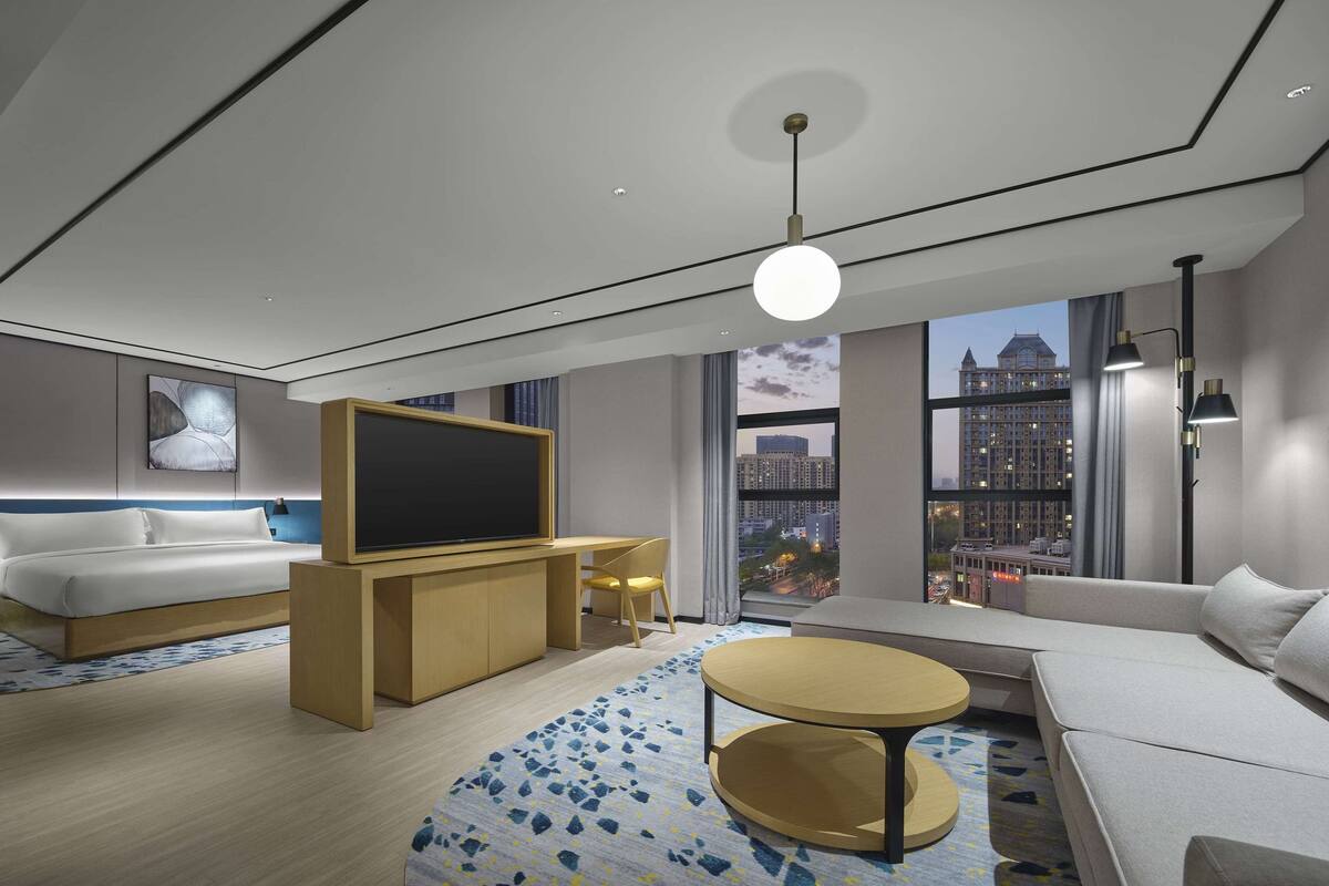 Habitación de hotel moderna con cama, sofá, televisión, escritorio y vista a la ciudad.