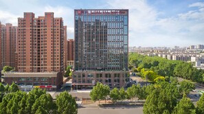Un edificio de gran altura con fachada de vidrio moderna, rodeado de edificios residenciales más bajos y un parque arbolado.