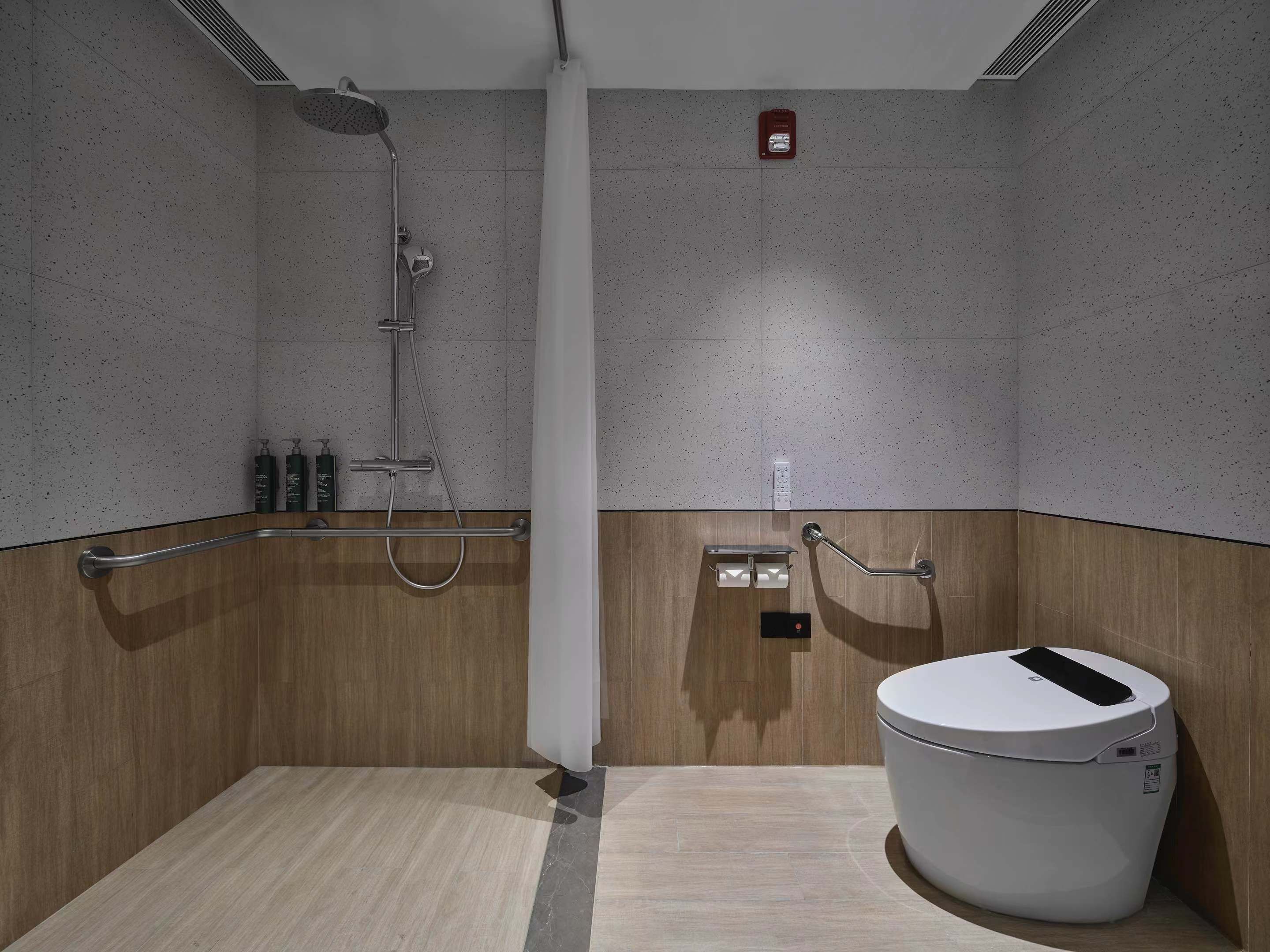 A modern bathroom with a shower, toilet, and handrails.
