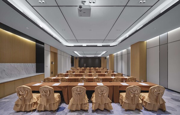 Uma sala de conferências com várias mesas e cadeiras, uma tela grande e um projetor.