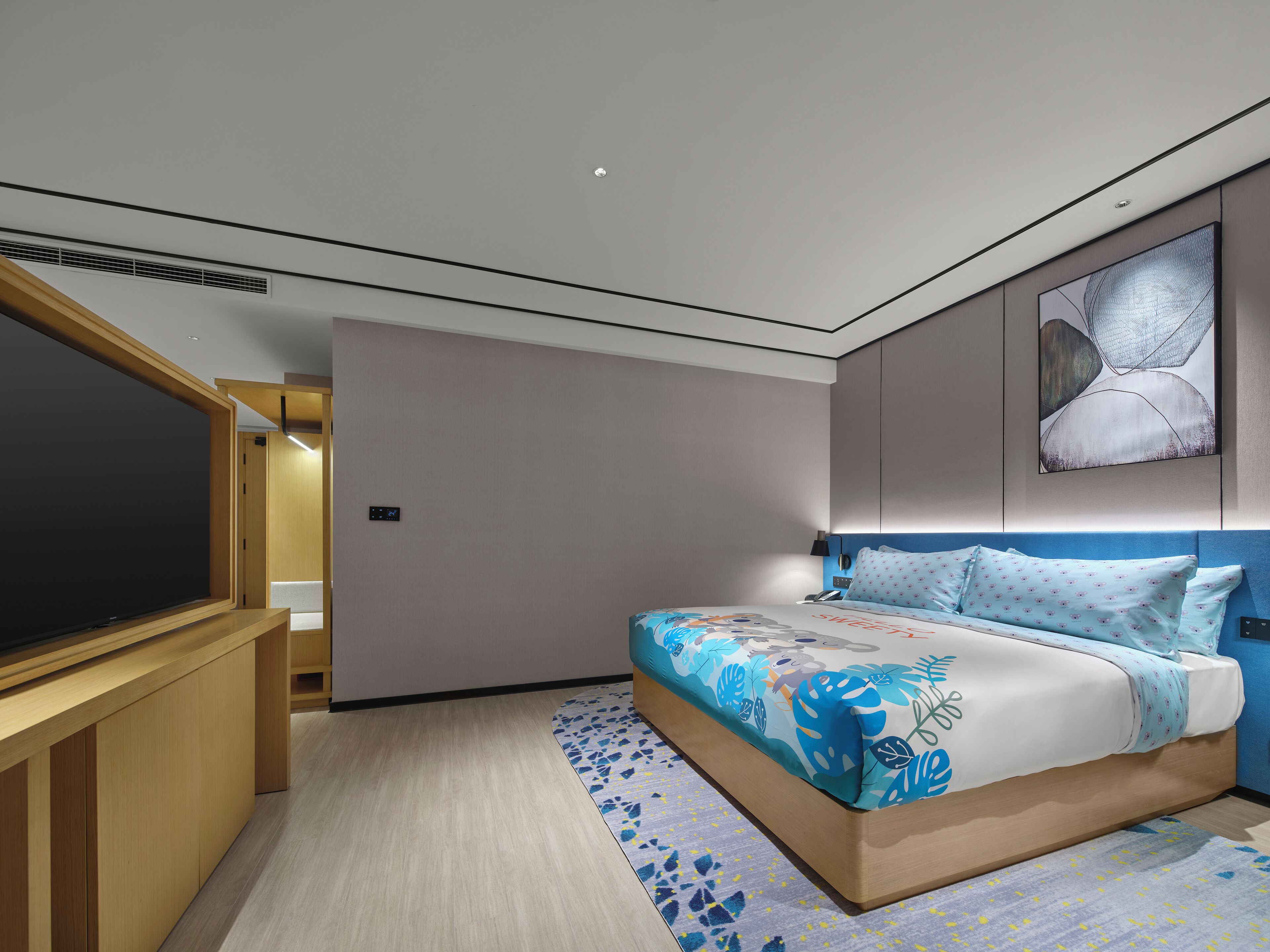 A modern hotel room with a large bed, a TV, and a small desk.