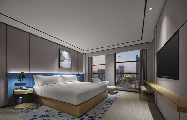 Habitación de hotel moderna con una cama grande, un escritorio, una silla, un televisor y vistas a la ciudad.