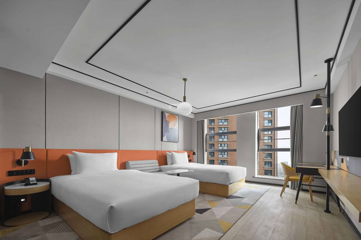 Una habitación de hotel moderna con dos camas, un escritorio, una silla y un ventanal con vistas a la ciudad.