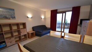 Une pièce comprenant un lit, un canapé, une petite table et un téléviseur. Il y a une fenêtre avec des rideaux et une vue sur l’extérieur.
