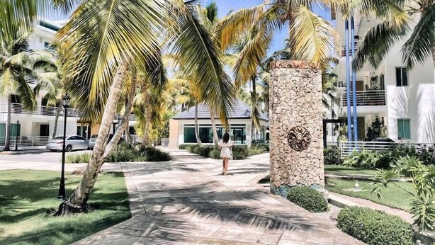Ein von Palmen gesäumter Weg, der zu einem Gebäude mit einer Steinsäule und einem Balkon führt.