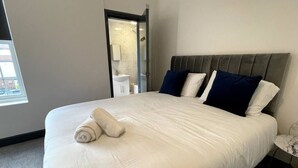 Ett hotellrum med en stor säng, ett nattduksbord, ett fönster och ett badrum som syns genom en öppen dörr.