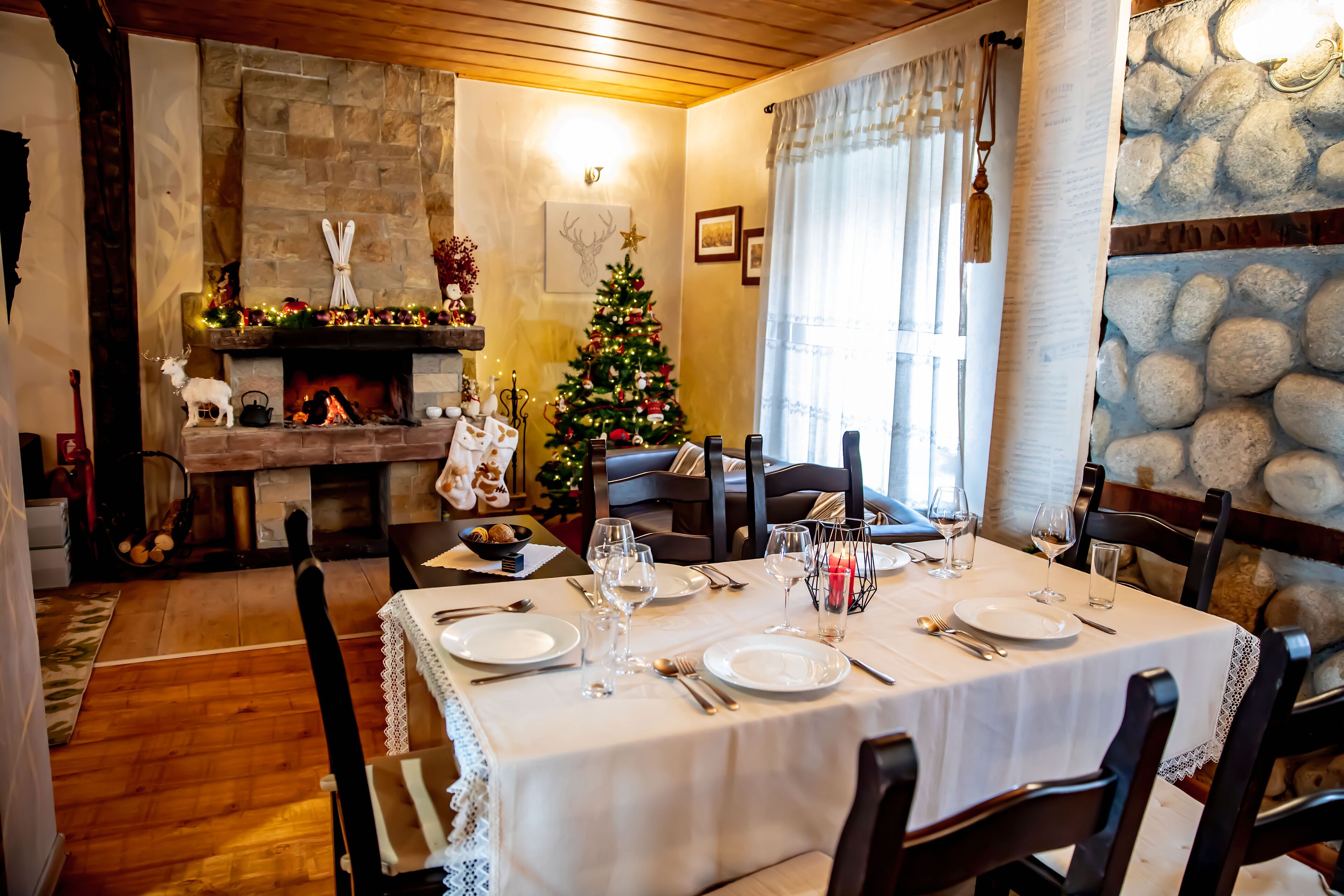 Uma sala de jantar com lareira de pedra, uma árvore de Natal e uma mesa posta para quatro pessoas.