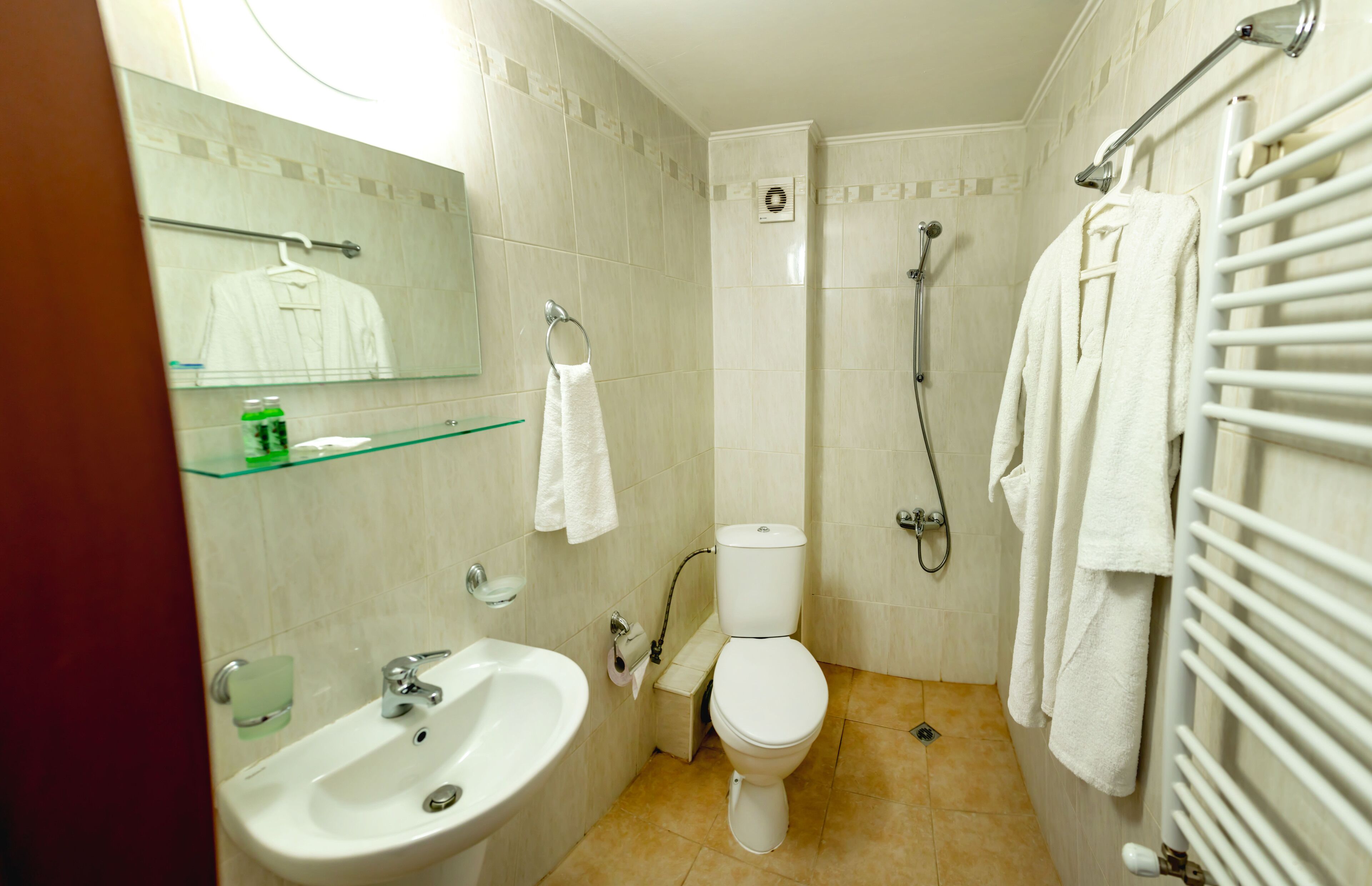 Une salle de bain équipée d’un lavabo, de toilettes et d’une douche. On y trouve également un porte-serviettes et une étagère en verre.