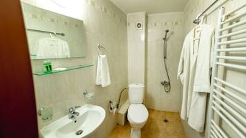 Une salle de bain équipée d’un lavabo, de toilettes et d’une douche. On y trouve également un porte-serviettes et une étagère en verre.