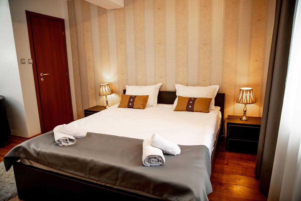 A neatly made bed with white and brown pillows, two bedside lamps, and a wooden door.