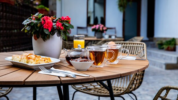 Une table ronde en bois, sur laquelle se trouvent une assiette de nourriture, une théière, un verre de thé et une tasse de café.