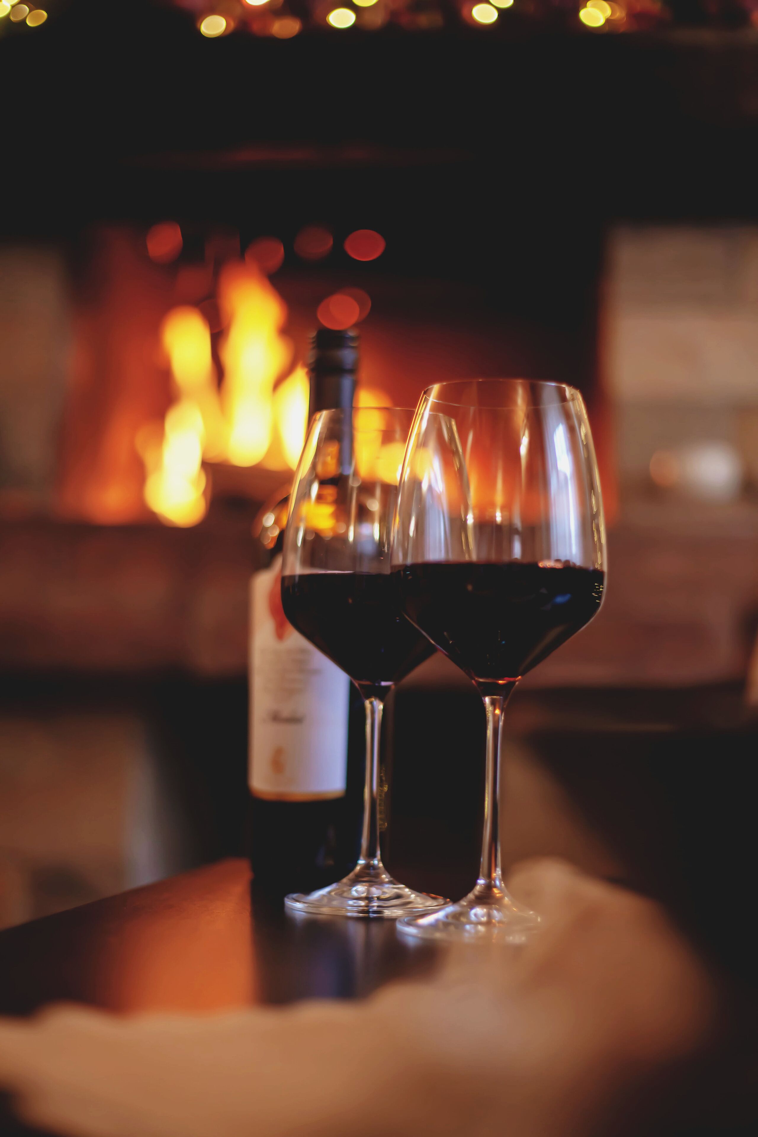 Two wine glasses on a table with a blurred background of a fireplace.