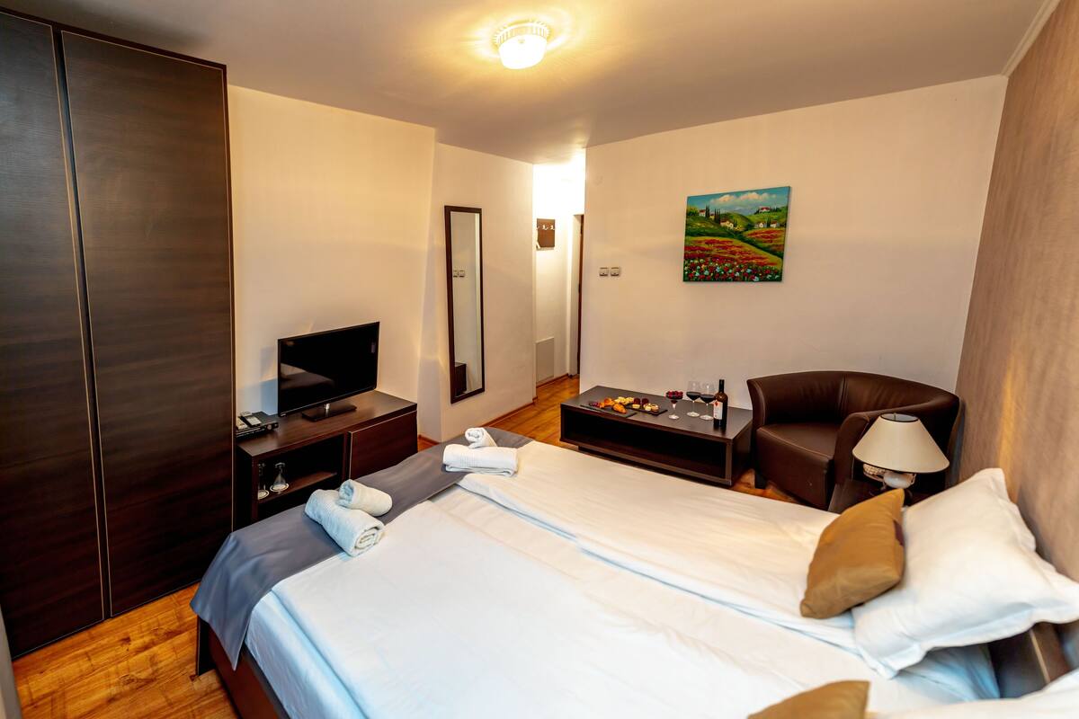 A hotel room with a bed, a television, a desk, a chair, and a painting on the wall.
