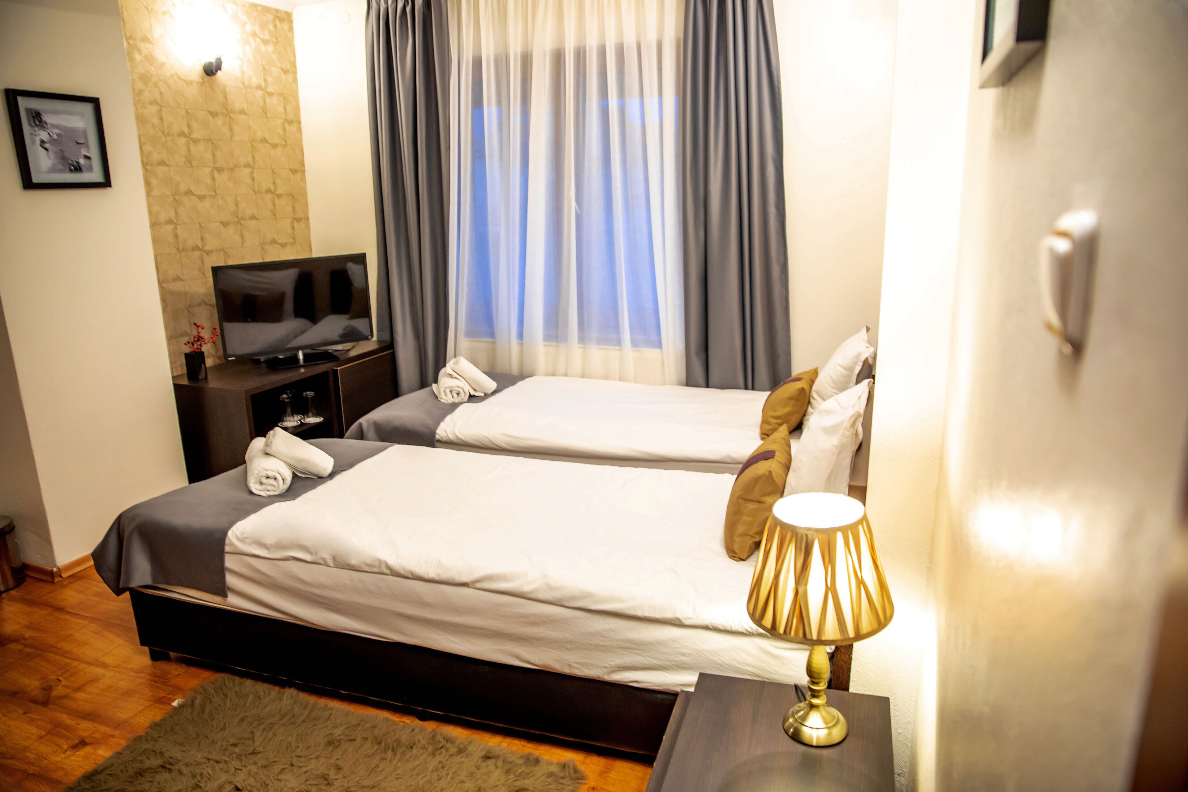 A hotel room with two beds, a TV, a lamp, and a window with curtains.