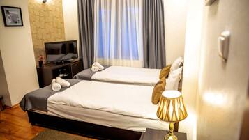 A hotel room with two beds, a TV, a lamp, and a window with curtains.