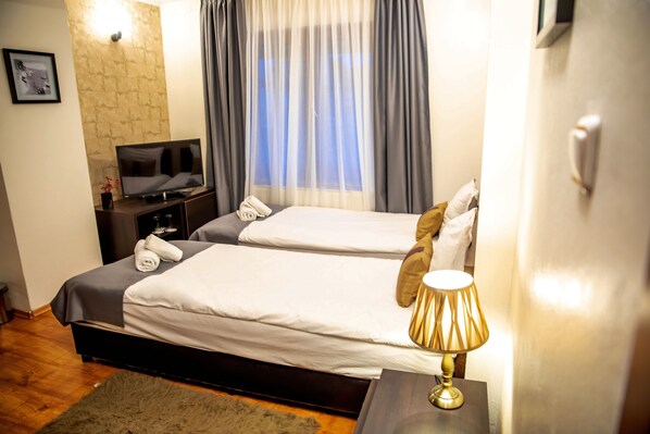 Habitación de hotel con dos camas, televisor, lámpara y ventana con cortinas.
