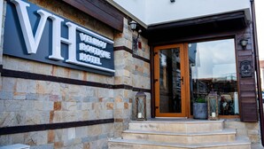 L’entrée d’un hôtel, avec une façade en pierre, une grande enseigne indiquant « HÔTEL VELINOV » et une porte en bois, accessible par quelques marches.